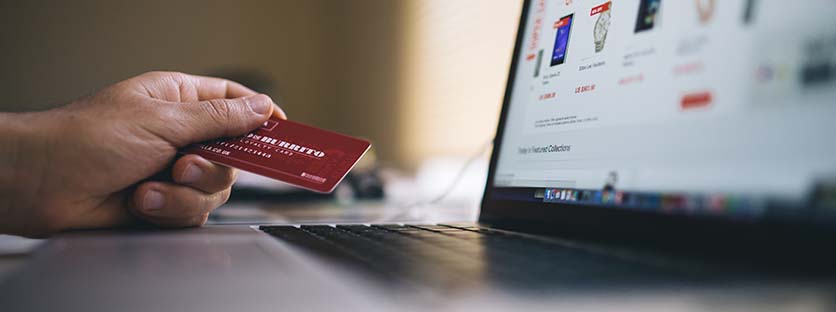 image of an open laptop with a shopping site open and a hand holding a credit card