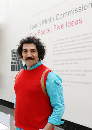 Michael Rakowitz smiling next to the Lamassu wearing a red sweater vest