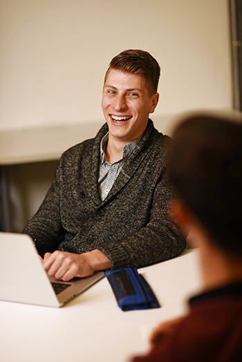 Evan Taylor on his laptop, laughing during a discussion with someone else